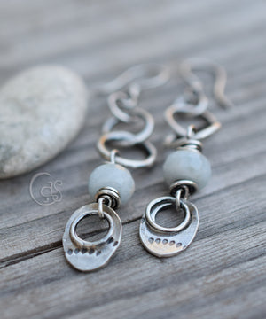 silver charm earrings with pale blue gemstones on a wood background with a white stone on the left. 