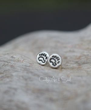 Silver post earrings with a bear paw motif on a wood background. 