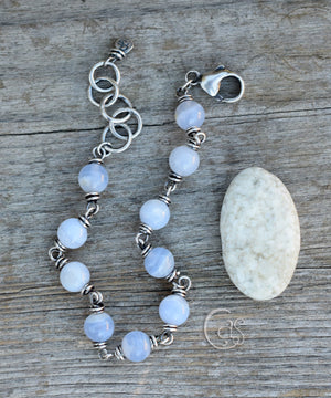 Round blue stone beaded silver bracelet next to a white and gray stone sitting on a wooden background. 