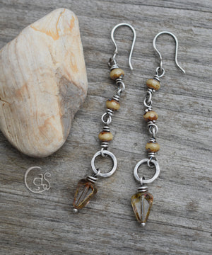 Silver earrings with beige glass beads and small silver rings on a wood background next to a pale stone. 