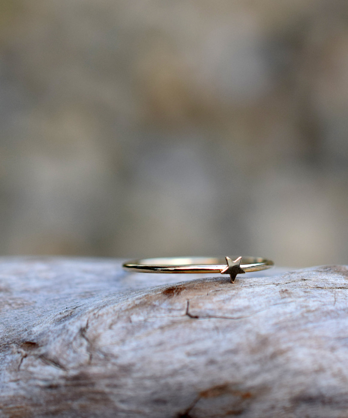 Single gold ring band with a star sitting on a piece of wood. The background is blurred out. 