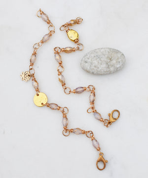 Two gold and glass beaded bracelets on a white background next to a gray rock. 