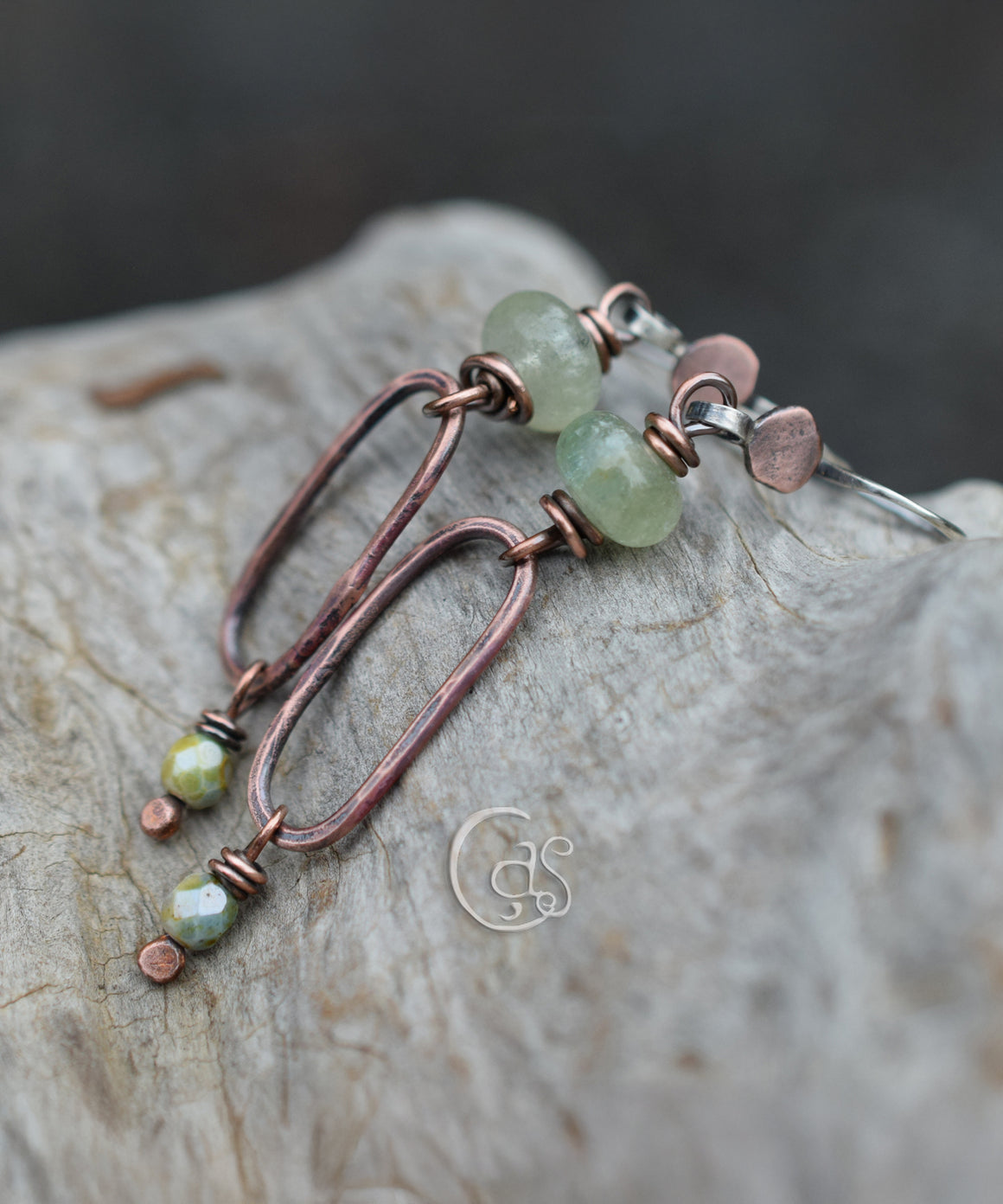 Green beaded copper earrings with oval hoops on a wood background. The earrings have small faceted green bead dangles at the bottom. 