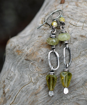 Green garnet silver hoop earrings with small loop rings on a wood background. 