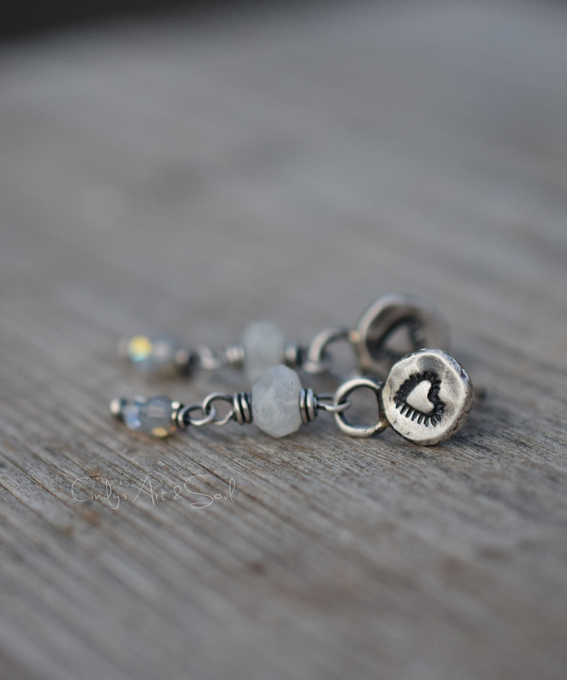 Silver Moonstone Post Earrings with gray sparkling beads on a wood background. The silver earrings have a heart design. 