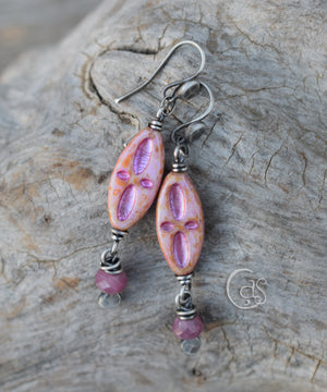 Pink and gold glass earrings with ruby dangles in sterling silver on a wood background. 