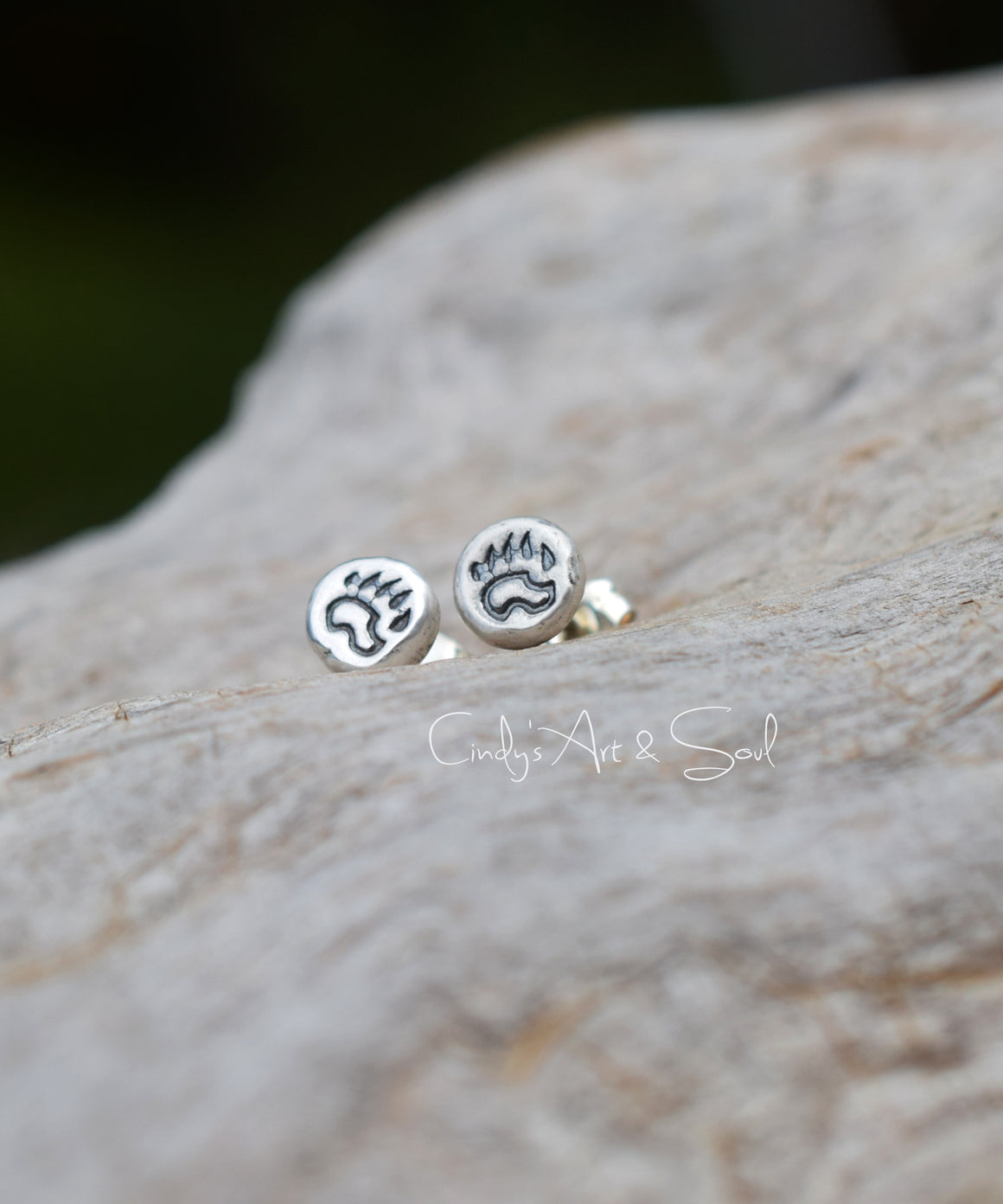 Silver post earrings with a bear paw image on them, on a wood background. 