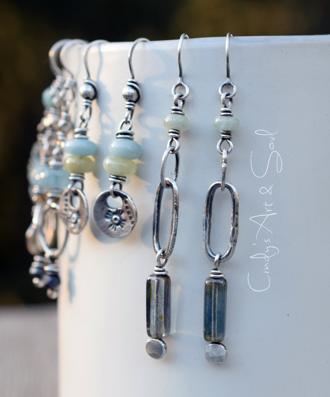 Several sets of silver beaded earrings hanging from a white cup. 