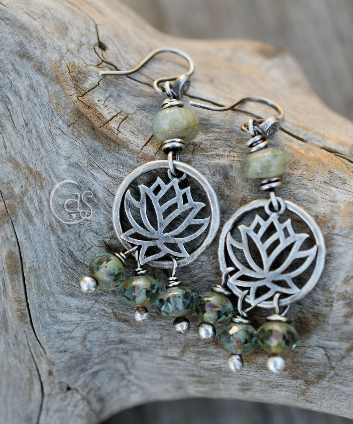 Silver hoop earrings with silver lotus charms and green beads on a piece of wood. 