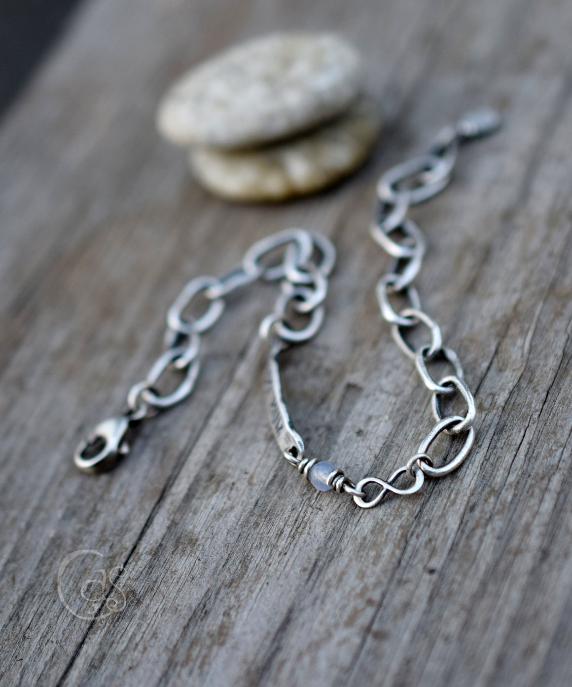 Solid silver chain bracelet with blue lace agate stone and infinity charm on a wood background with stones stacked. 