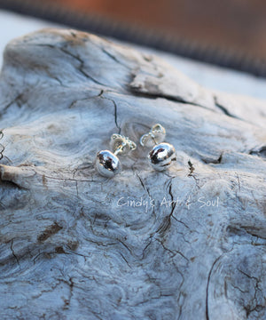 Silver ball earrings sitting on driftwood. 